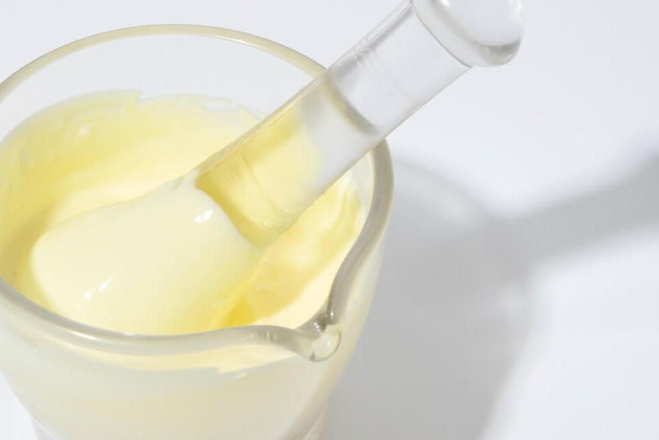 White background with a glass measuring cup fillled with yellow paste and a glass pestle